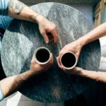 View from above of two people sitting at a round grey table drinking coffee